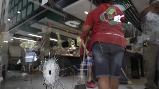 Empleados del supermercado Único limpian los restos de vidrios que quedaron en el piso tras la balacera contra el local.