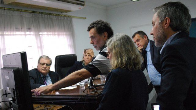 César Román, frente al tribunal, indica en un plano de la delegación de la Policía Federal el lugar en donde estuvo detenido ilegalmente y la sala de torturas. Lo rodean la fiscal Milagros Squivo, el abogado querellante Marcelo Boeykens y Lucía Tejera, de fondo el abogado defensor José Ostolaza.    